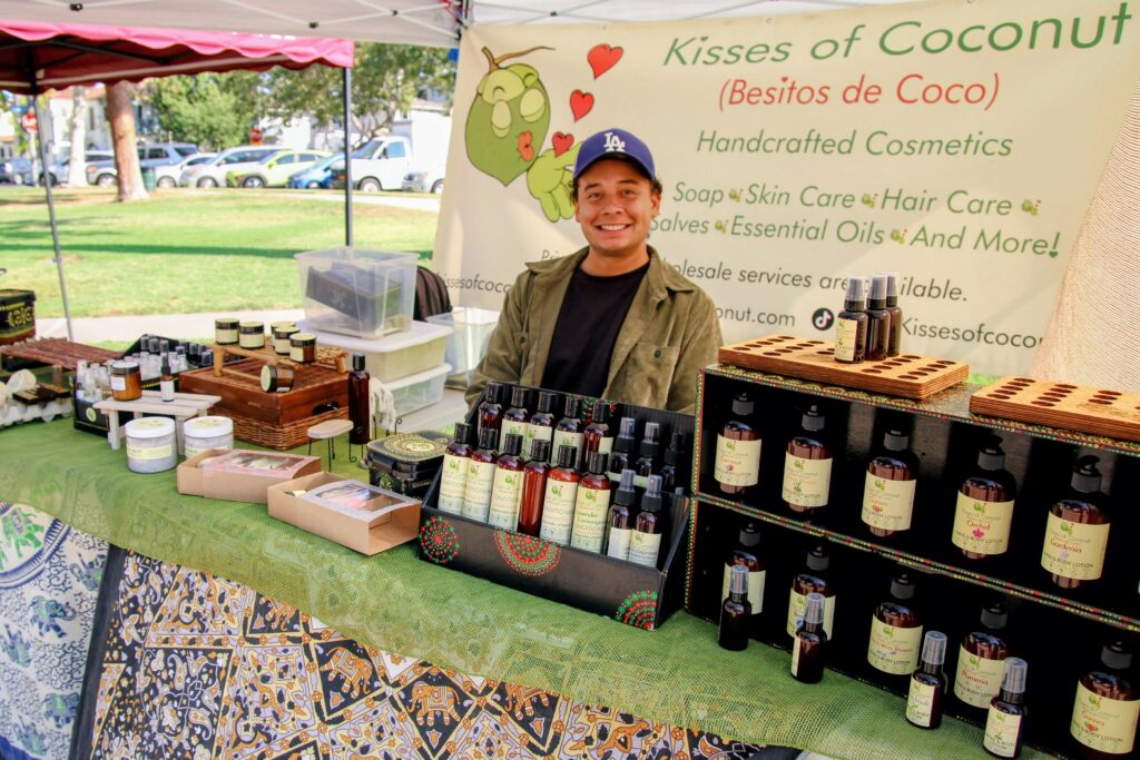 Market booth with bottled skincare and body care products displayed on tables under a tent.