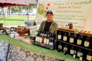 Market booth with bottled skincare and body care products displayed on tables under a tent.