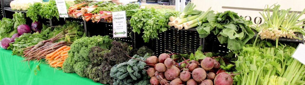 Display of fresh vegetables at a market stall including beets, carrots, kale, celery, leeks and cabbage.