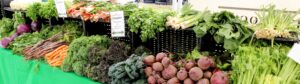 Display of fresh vegetables at a market stall including beets, carrots, kale, celery, leeks and cabbage.