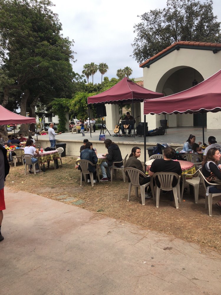 Outdoor market stage with musician, tents, tables, and chairs at Bixby Park