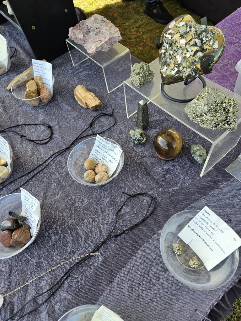 Assorted crystals, minerals and polished stones displayed in bowls and on clear acrylic risers on a patterned tablecloth.