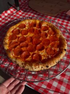 Fresh pepperoni pizza on a wire cooling rack over a red and white checkered tablecloth.