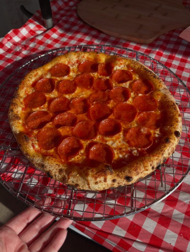 Fresh pepperoni pizza on a wire cooling rack over a red and white checkered tablecloth.